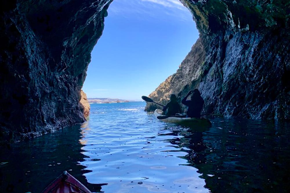 Two kayakers inside a sea cave on the Mendocino coast, looking out to open water